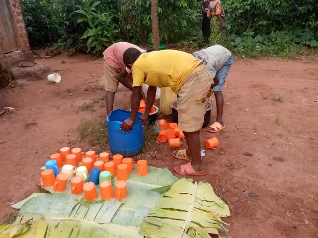 Boys washing enamel cups laid on banana leaves in the courtyard